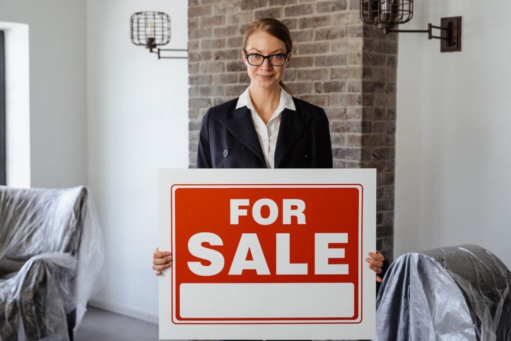 A real estate agent holding a 'for sale' sign.