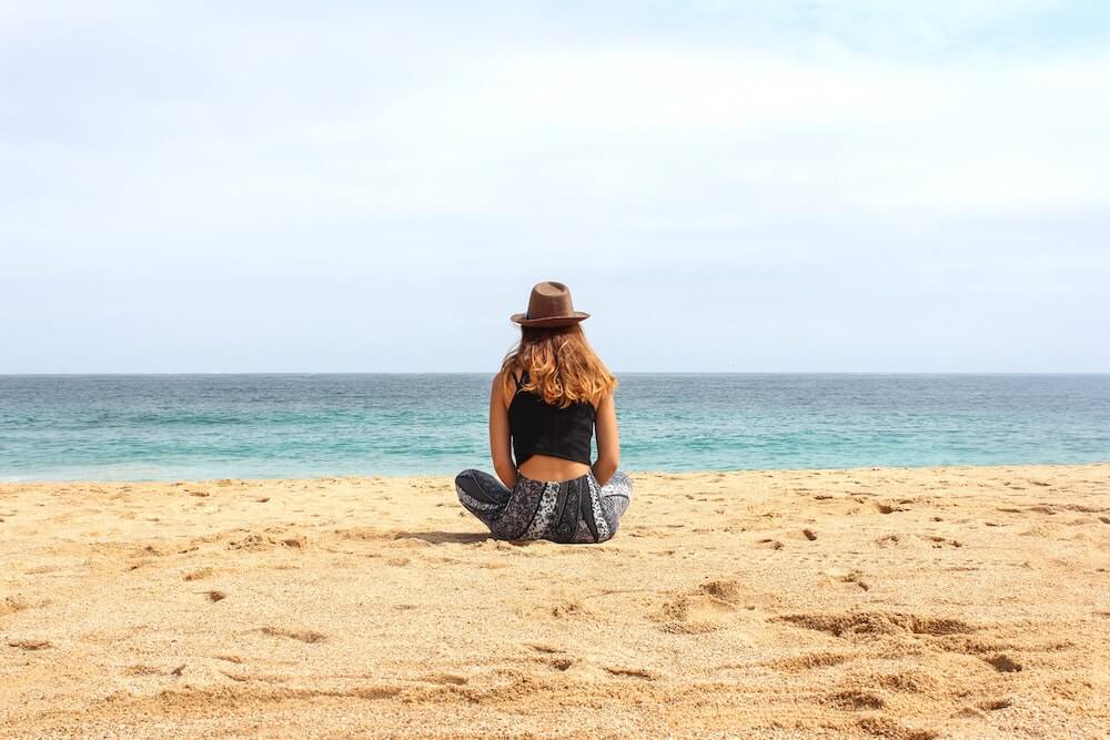 woman sitting on beach looking at ocean